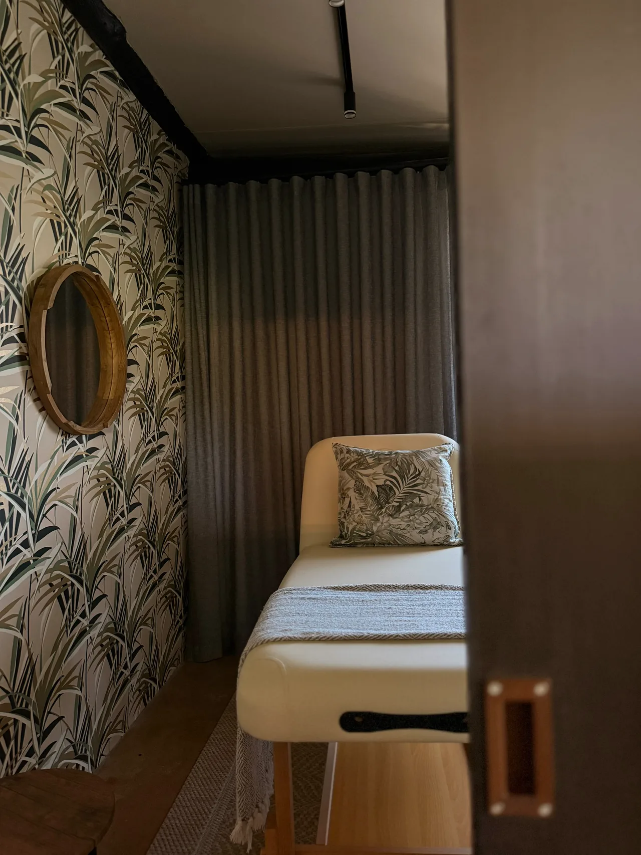 Garden suite — Treatment room with leaf wallpaper, a round mirror and a massage bed