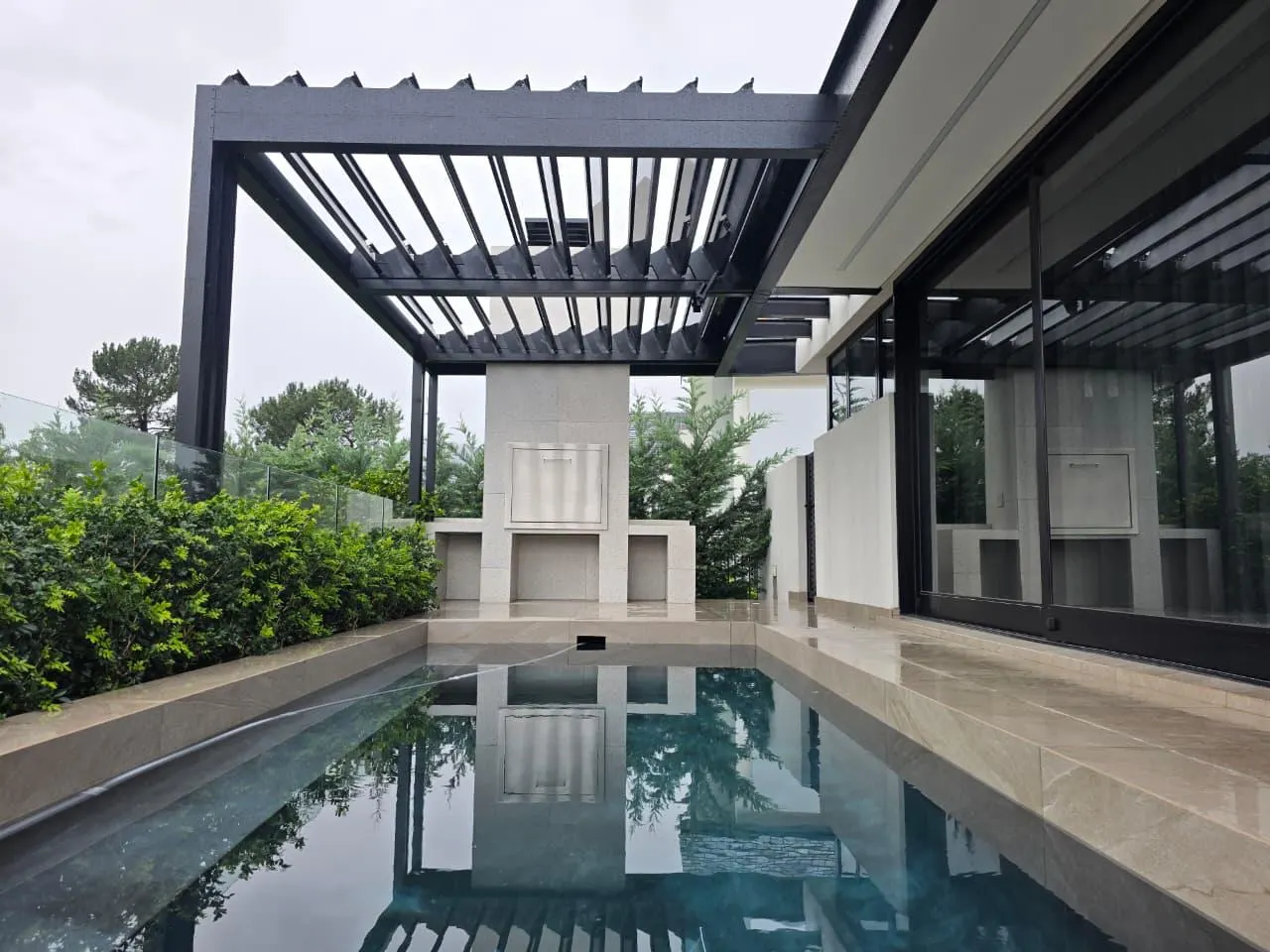 Black aluminium louvre pergola over a lap pool and white masonry boma