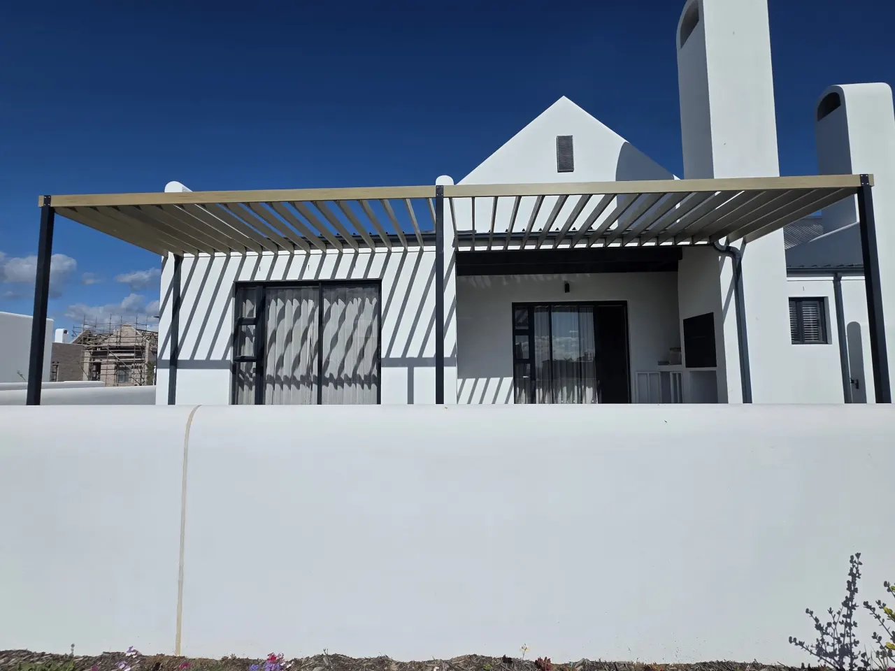 Slatted pergola shading the patio of a white Cape-style house