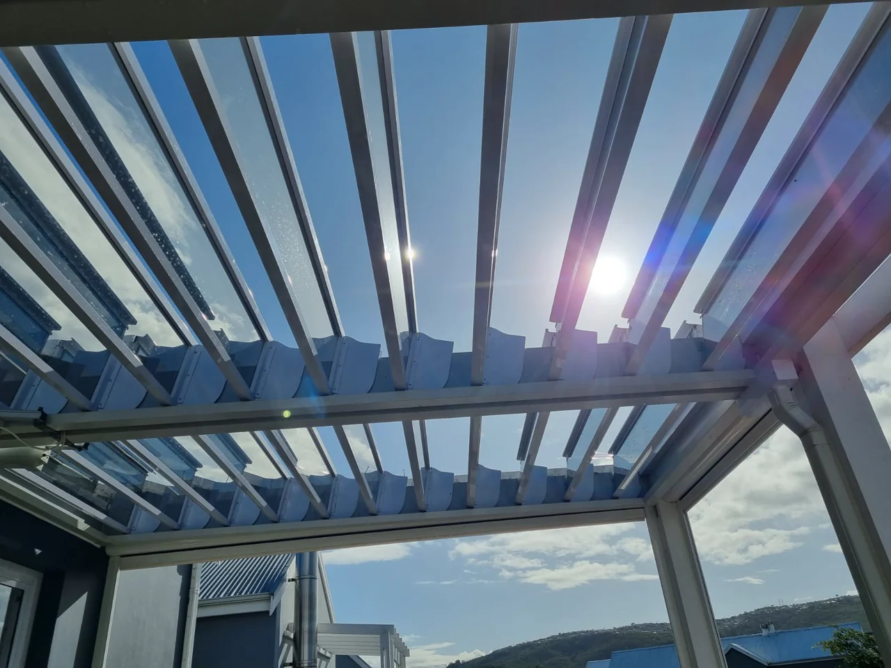 Sun shining through partly open glass louvre blades over a terrace