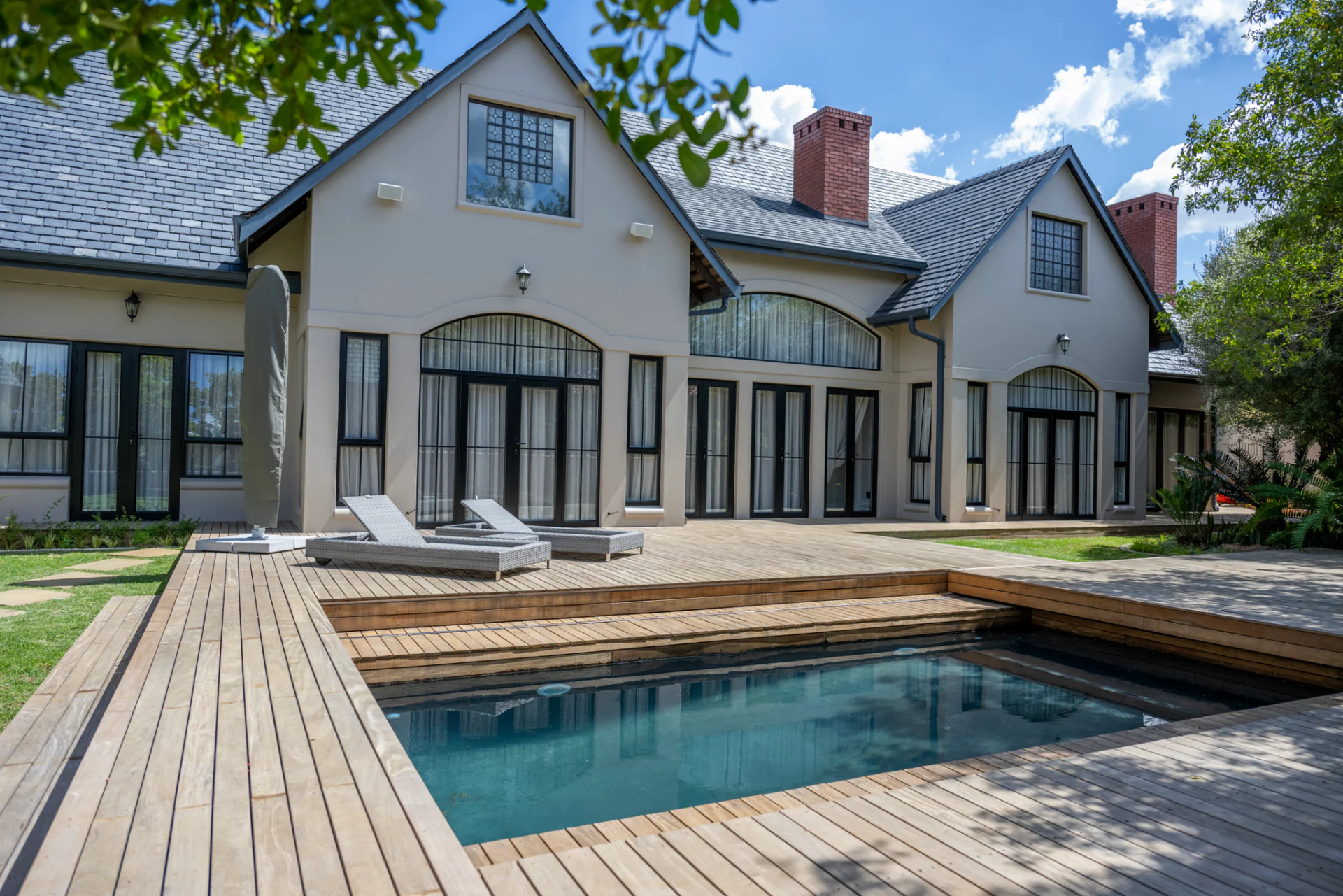 Slate-roofed home with a timber sliding deck partly open over the pool, and two loungers on the deck