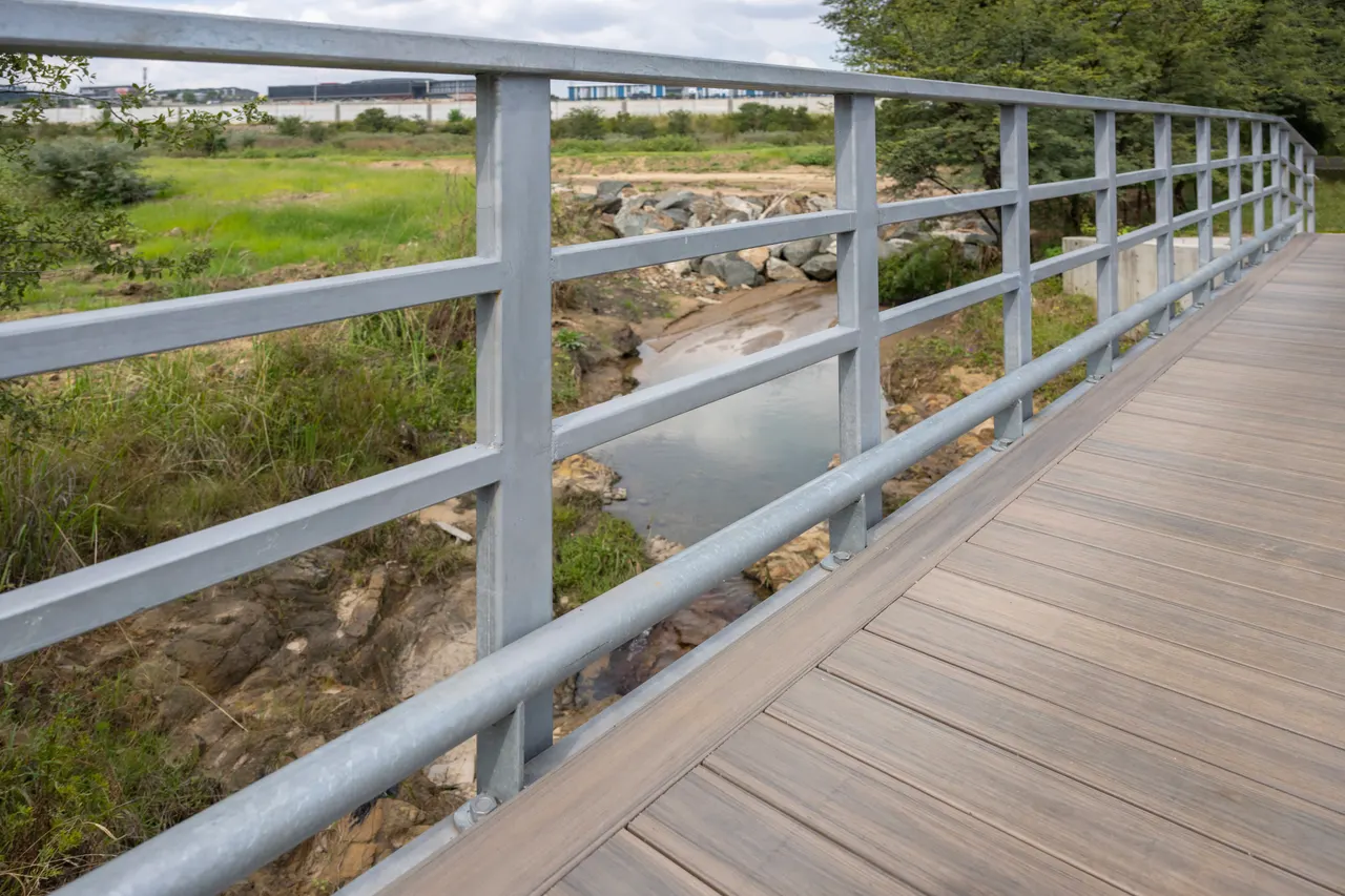 Timber bridge deck between galvanised steel railings above a river
