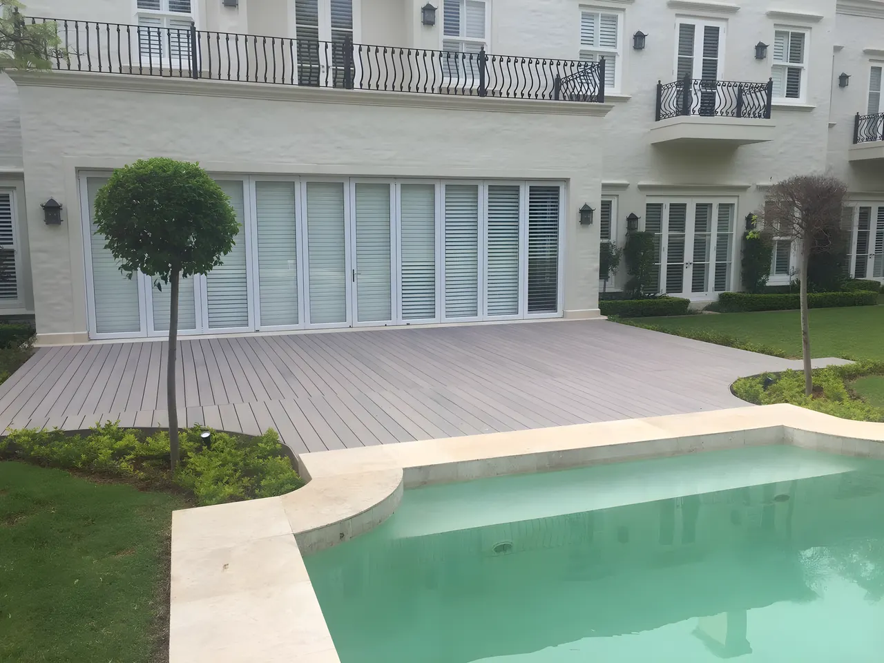 Composite pool deck with a clipped tree and garden beyond