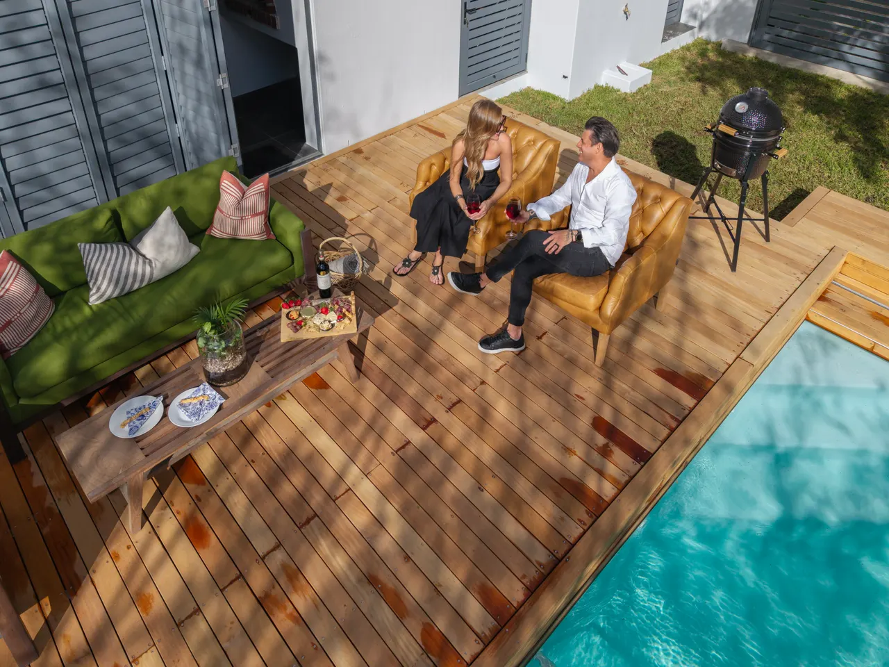 Aerial view of a timber sliding deck beside an open pool, with outdoor lounge furniture